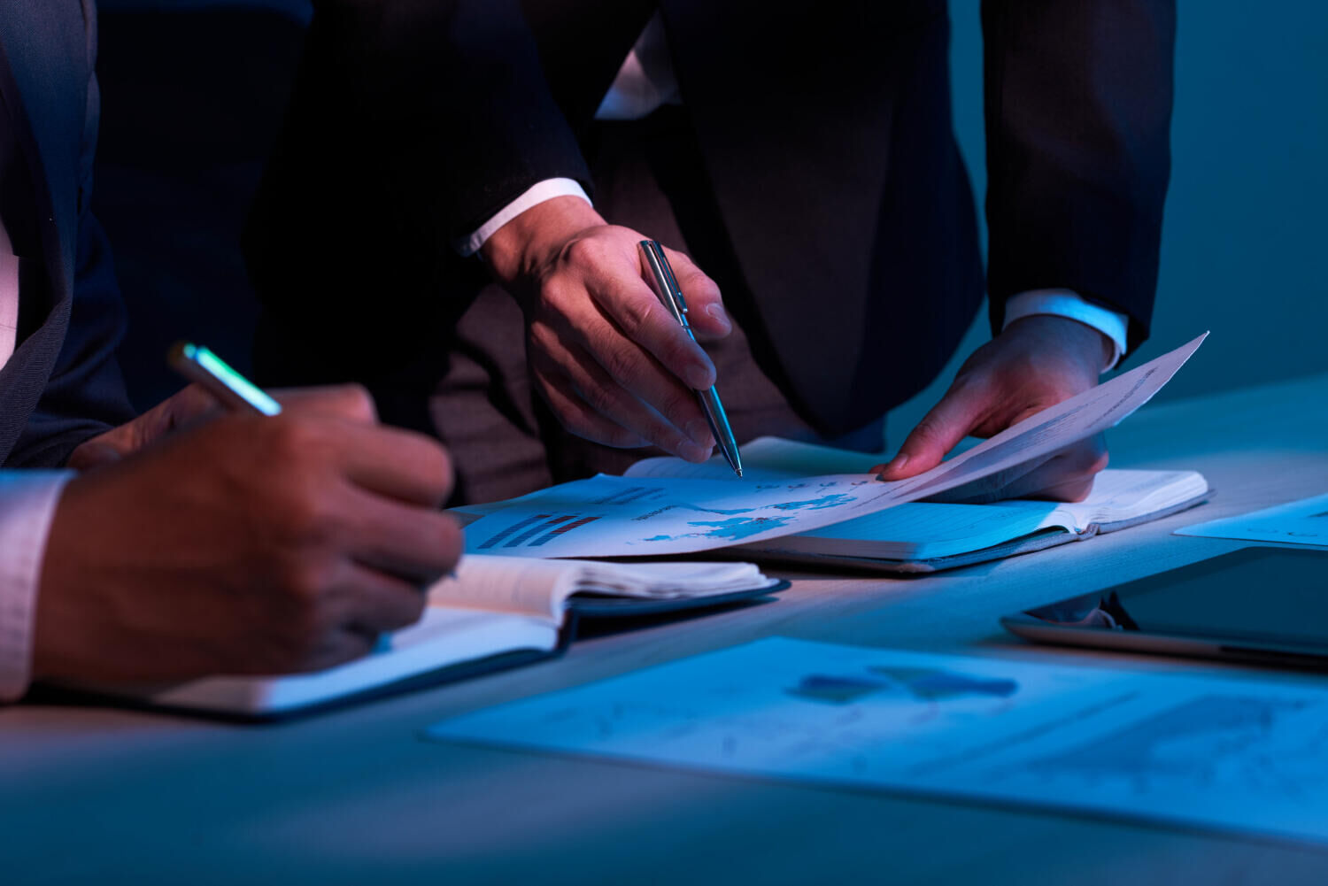 Dois profissionais de terno analisando documentos financeiros com gráficos