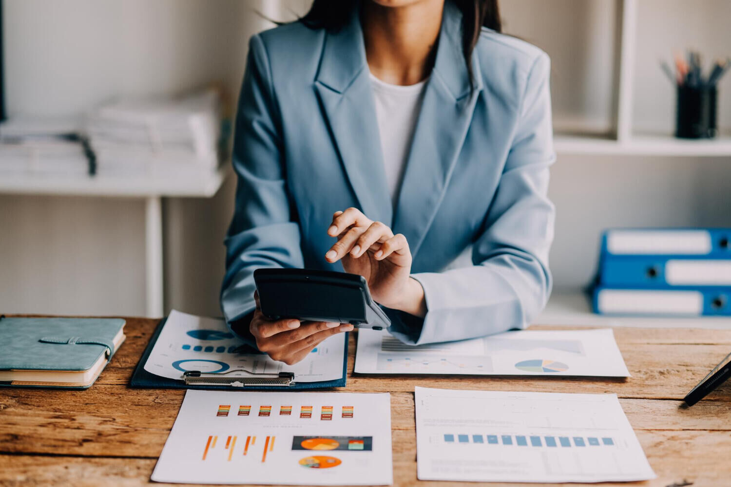Mulher de blazer usando calculadora sobre relatórios com gráficos