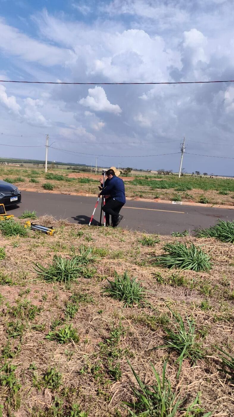 Técnico coletando pontos com bastão GNSS na borda de via em loteamento