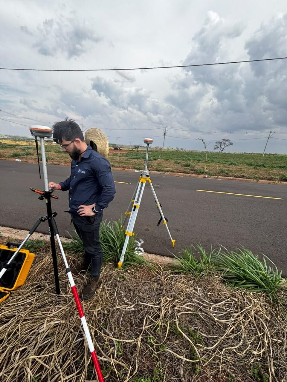 Técnico da RC Geo com coletora de dados ao lado de um receptor GNSS em via asfaltada