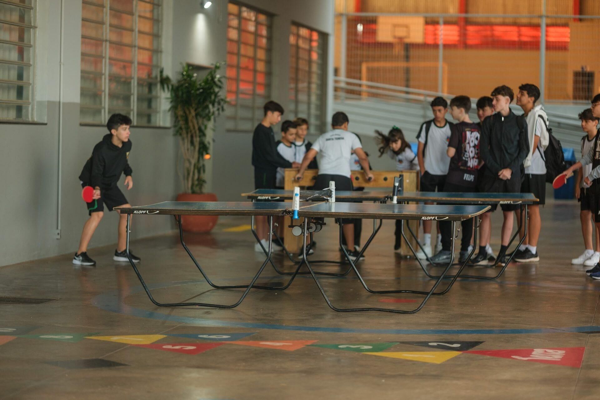 Alunos jogando tênis de mesa no pátio coberto