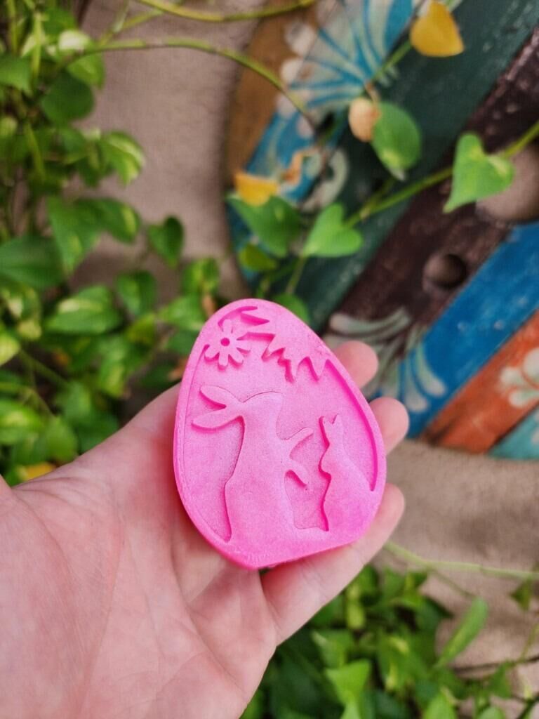 Sabonete rosa com coelhos em relevo na mão, entre folhas
