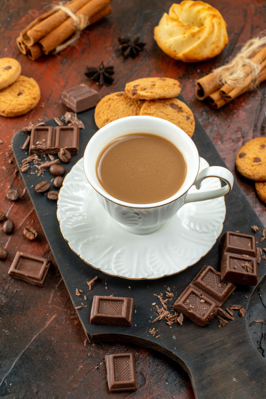 Imagem acima-vista-de-um-delicioso-cafe-em-copo-branco-na-tabua-de-madeira-biscoitos-limas-e-canela-barras-de-chocolate-em-fundo-de-cor-mista