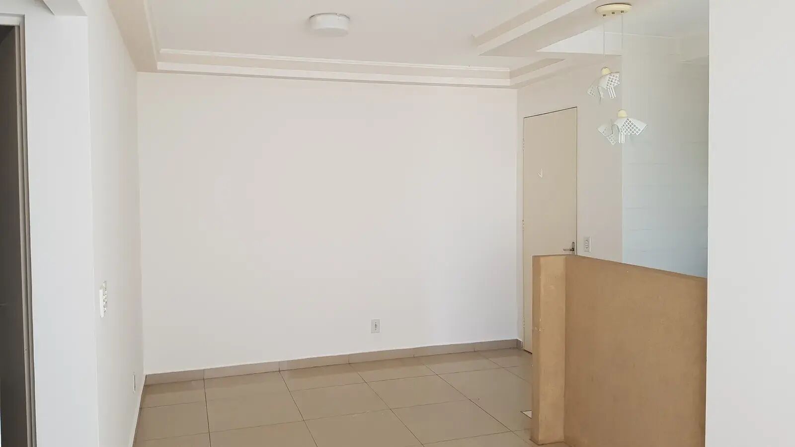Sala vazia com forro de gesso rebaixado, piso de porcelanato e meia parede de divisão com a cozinha