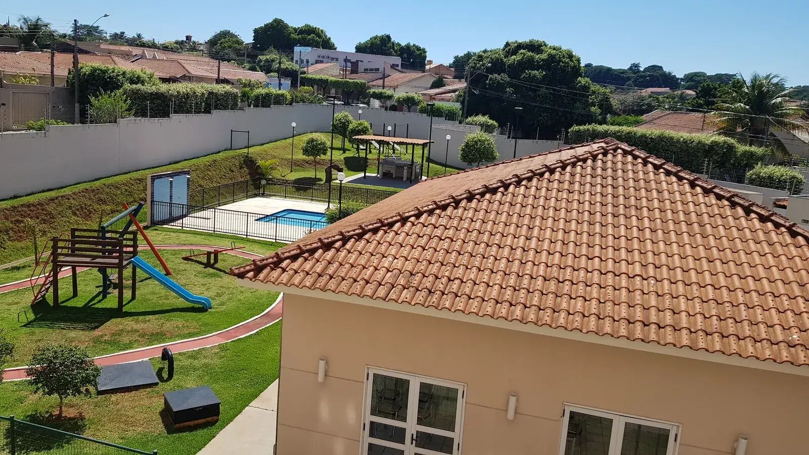 Vista de cima do condomínio com playground, piscina, quiosque de churrasco e telhado do salão de festas